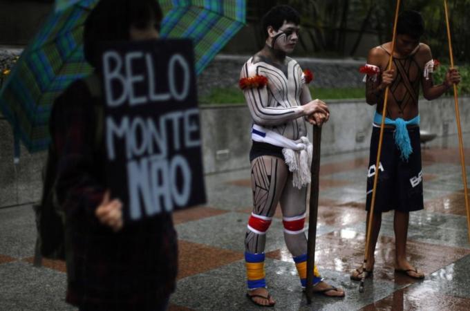 Brazilian indigenous men stand next to an environmental activist as he holds a banner that reads