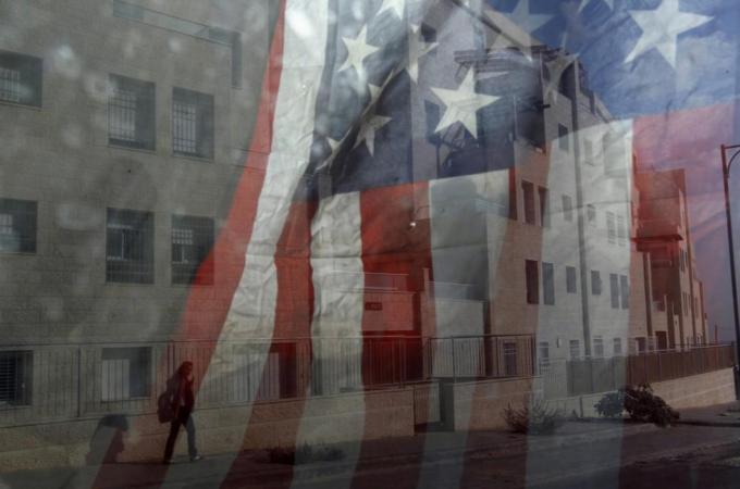 An Israeli woman is reflected in an American flags which is hung inside a bulldozer at a construction site in Givat Zeev.