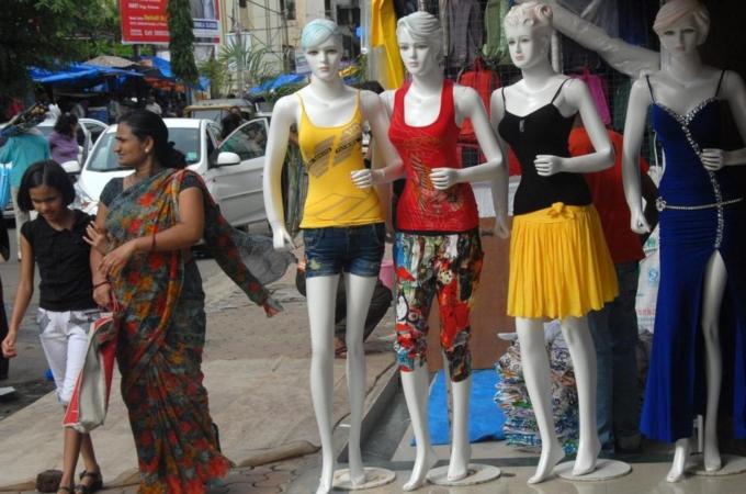 An Indian elderly woman walks past mannequins with western outfits displayed outside a roadside retail garment shop in Mumbai.