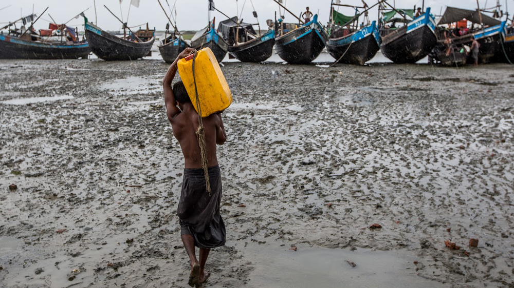A Rohingya deckhand carries a jerrican of water out to a boat about to leave for the Bay of Bengal. These days, rickety vessels ferry refugees to larger boats waiting offshore that fill up and continue on to Thailand [Jason Motlagh/Al Jazeera]
