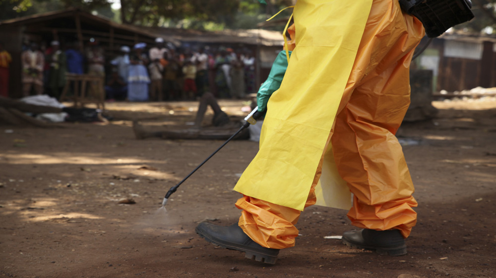 A crowd gathers around a motionless body in Forecariah, Guinea as a French Red Cross team disinfects the area [Misha Hussain/Thomson Reuters Foundation]