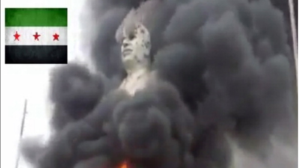 An image grab taken from a video uploaded on YouTube shows flames rising from a statue of late Syrian president Hafez al-Assad in al-Raqqa [AFP]