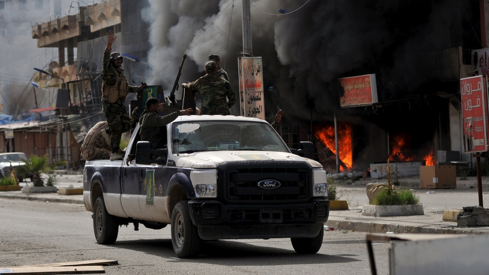 Members of Hashid Shaabi forces ride in a vehicle as smoke rises in shops at al-Qadisiya neighborhood, north of Tikrit