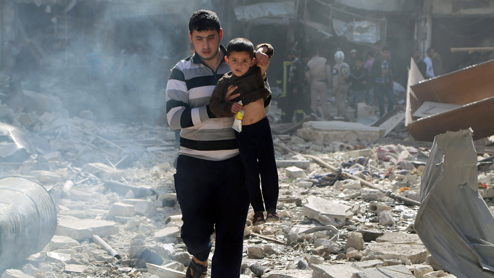 A man carries a boy over debris at a site damaged by what activists said was a barrel bomb dropped by forces loyal to Syria''s president Bashar Al-Assad in Aleppo''s al-Saliheen district