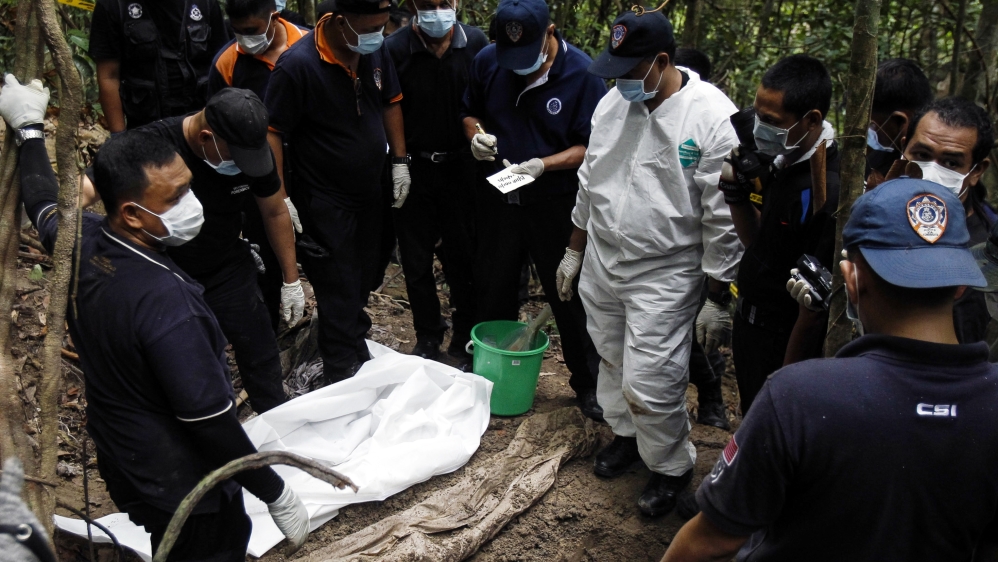 Malaysian police forensic team members inspect a freshly exhumed human body