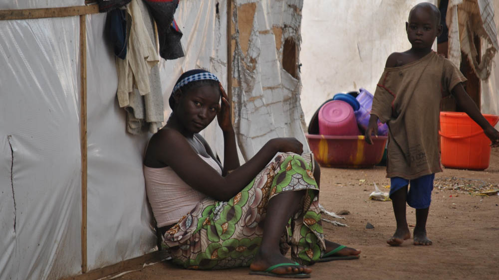 A woman sits in front of a tent provided by the IRC in Girei I government IDP camp in Yola [Fragkiska Megaloudi/Al Jazeera]