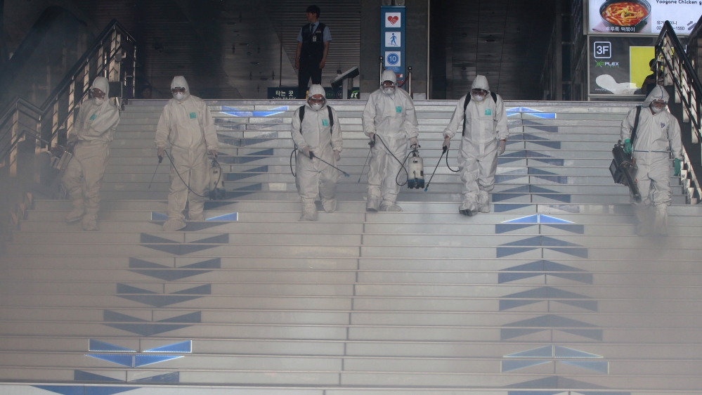 Workers wearing protective gears fumigate and spray antiseptic solution as a precaution against the spr