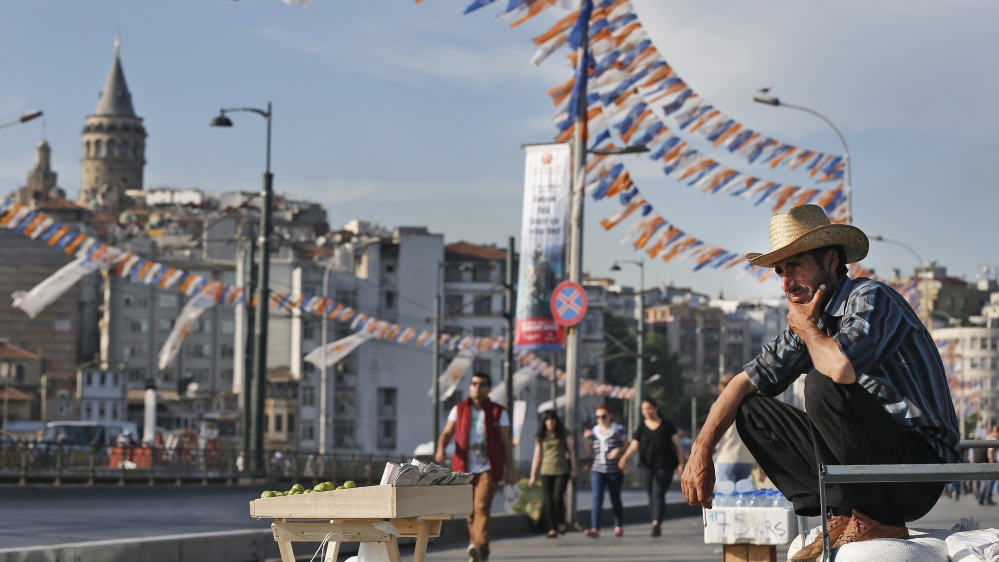 FILE - In this Tuesday, May 26, 2015 file photo, a street vendor is backdropped by the iconic Galata Tower and party flags and banners for the upcoming elections, as he waits for customers, in Istanbu