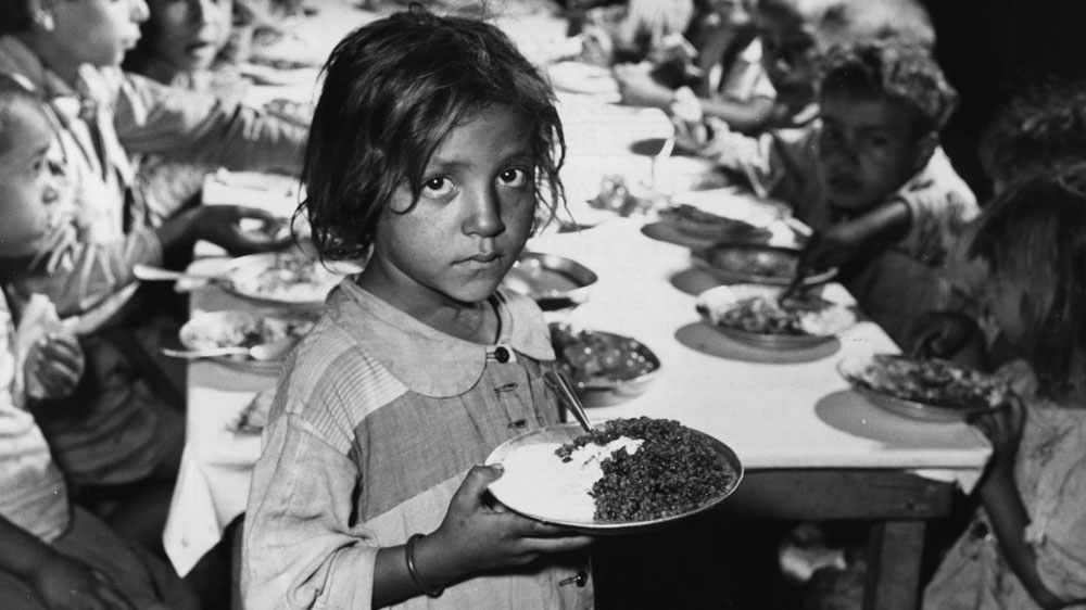 A Palestinian girl receives food at a refugee camp run by the UNHCR in Jordan, circa 1955 [Getty Images]