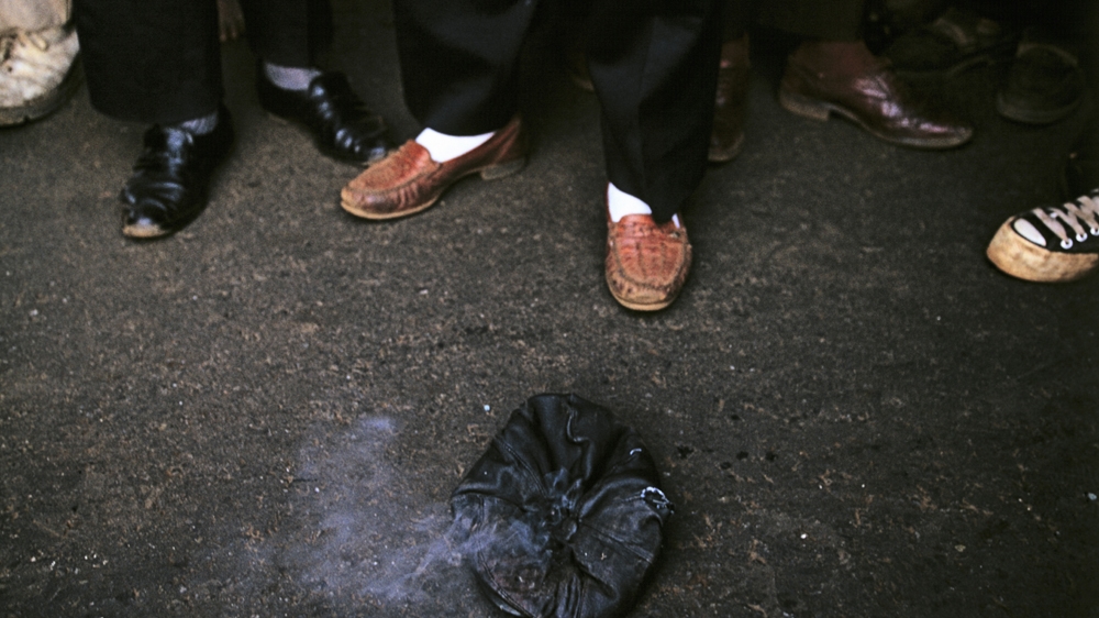 In this photograph taken in 1994, ANC supporting activists stand above a cap, still smoking from a point-blank range gunshot that killed one of their Self Defence Unit comrades while he was watching the FIFA World Cup. The shot was fired by a member of the Inkatha Freedom Party [Greg Marinovich]