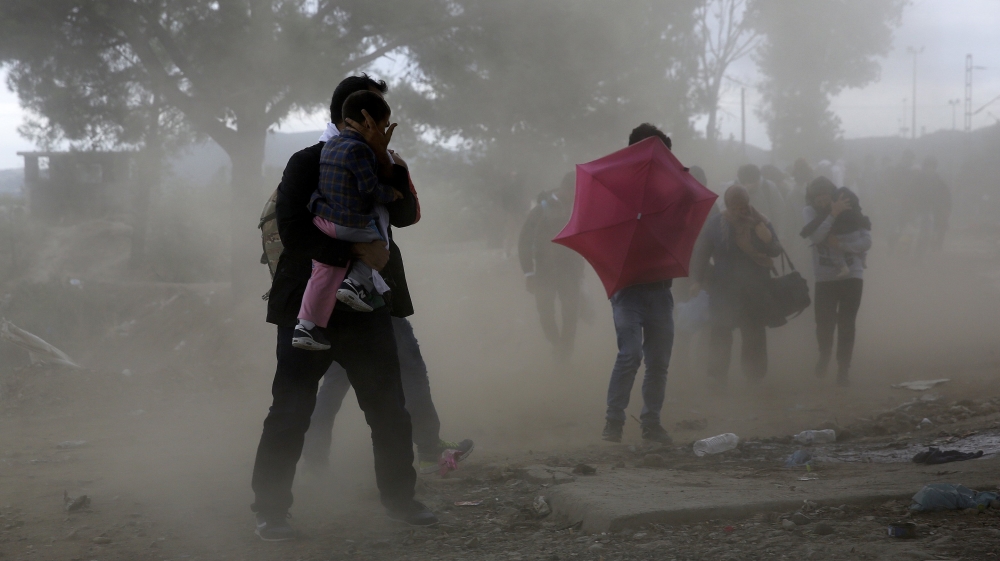 Syrian refugees try to protect themselves from gusts of wind and dust as they cross Greece''s border with Macedonia