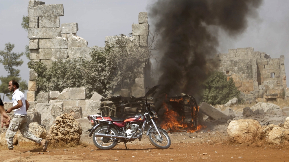 A man runs past a burning military vehicle at a base controlled by rebel fighters from the Ahrar al-Sham Movement in the southern countryside of Idlib