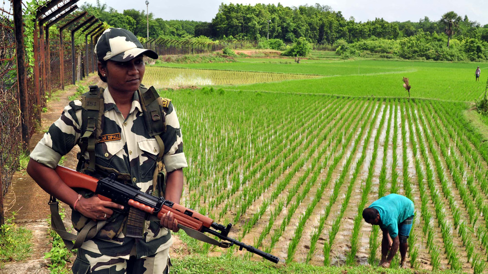 A farmer sows crops on his land outside India's well-guarded fence [Pinaki Das/Al Jazeera]