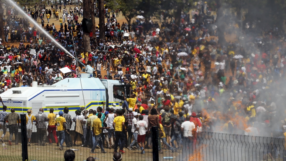 A demonstrator hangs on to a police water cannon during a protest over planned increases in tuition fees outside the Union building in Pretoria