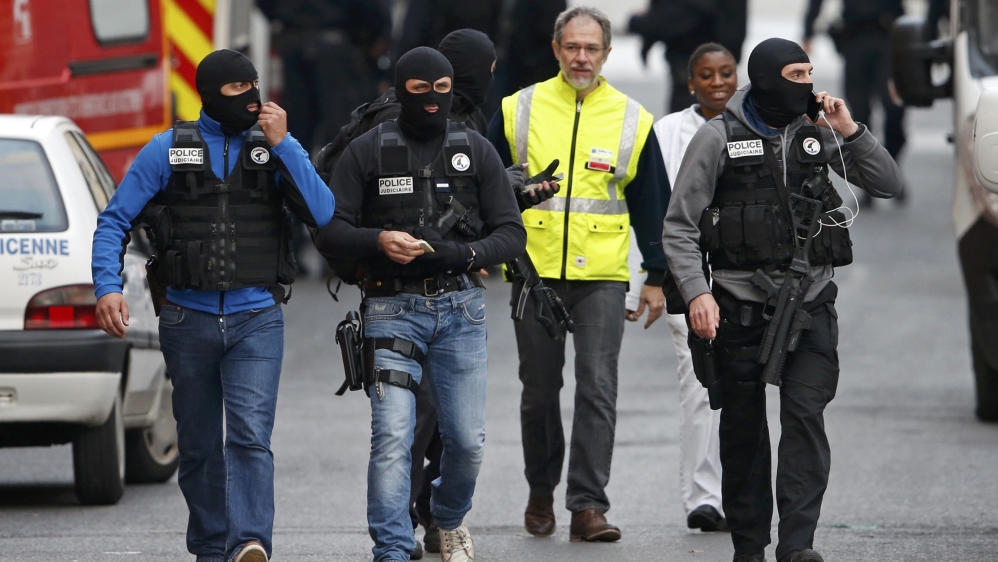 Masked French judicial police unit members walk at the scene of the raid in Saint-Denis