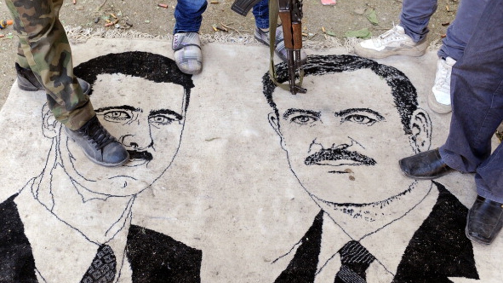 Syrian opposition fighters standing on a mat bearing drawings of Syrian President Bashar al-Assad and his late father Hafez [AFP]
