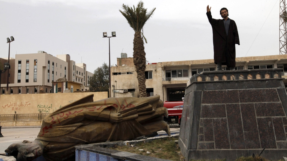 File photo of a man raising his hand as he stands on the spot where the statue of Hafez Al-Assad used to be in Raqqa province