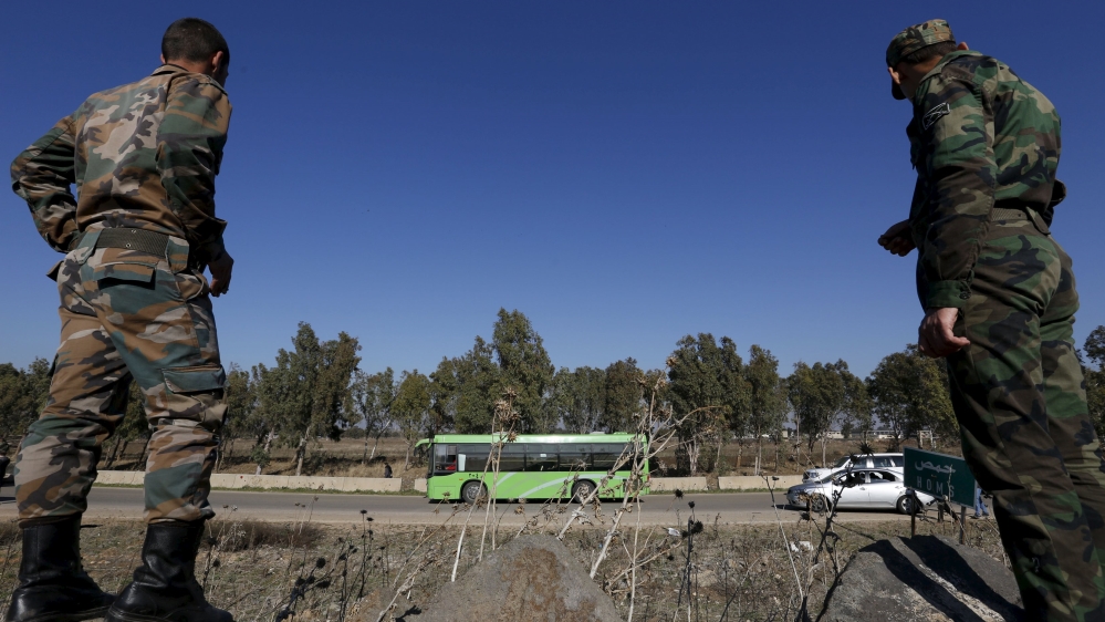 Syrian Army forces look on as buses leave district of Waer during a truce between the government and rebels, in Homs