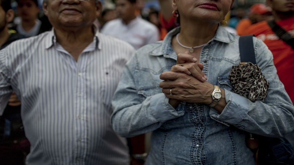 An opposition supporter grips a crucifix as she listens to a speech at an opposition rally [Alejandro Cegarra/Al Jazeera]