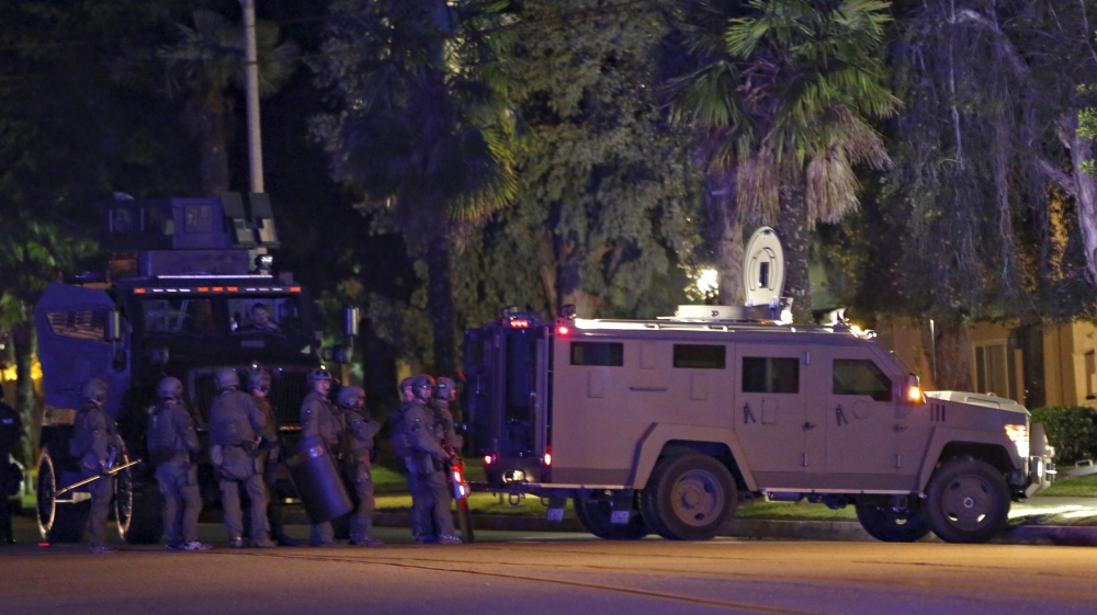 Police officers and their vehicles line the street outside the house of one of the suspects in a mass shooting in Redlands, California