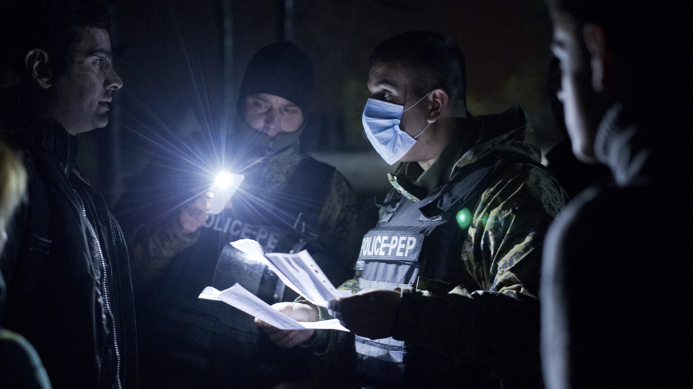 A police officer on the Greece-Macedonia border checks the documents of newly arrived refugees, early in the morning [Anna Psaroudakis/Al Jazeera]