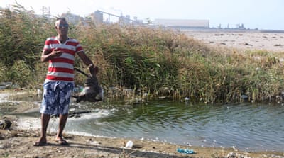 Sadeg Ghauma shows a dead bird in a puddle of dirty seawater on the beach of Chott Esselam, near the phosphate plant [Thessa Lageman/Al Jazeera]