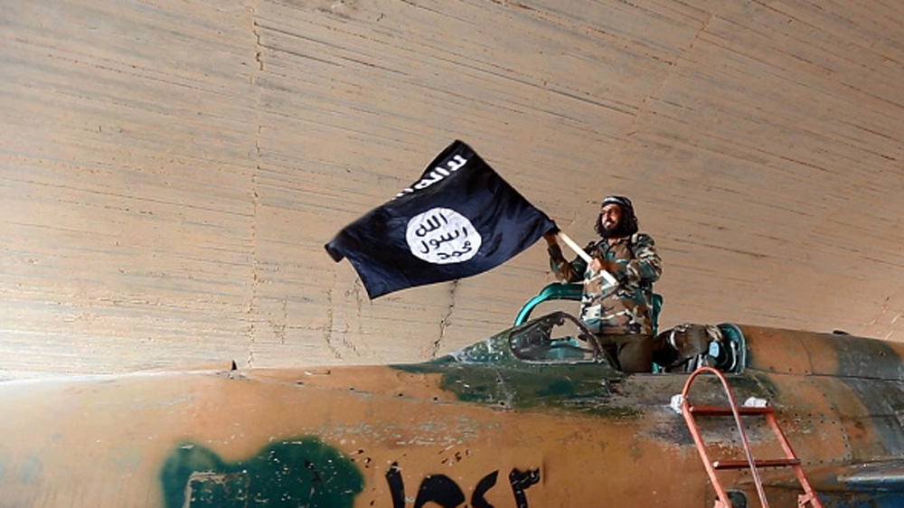 ISIL fighter waving a flag while standing on captured government fighter jet in Raqqa, Syria [Getty]