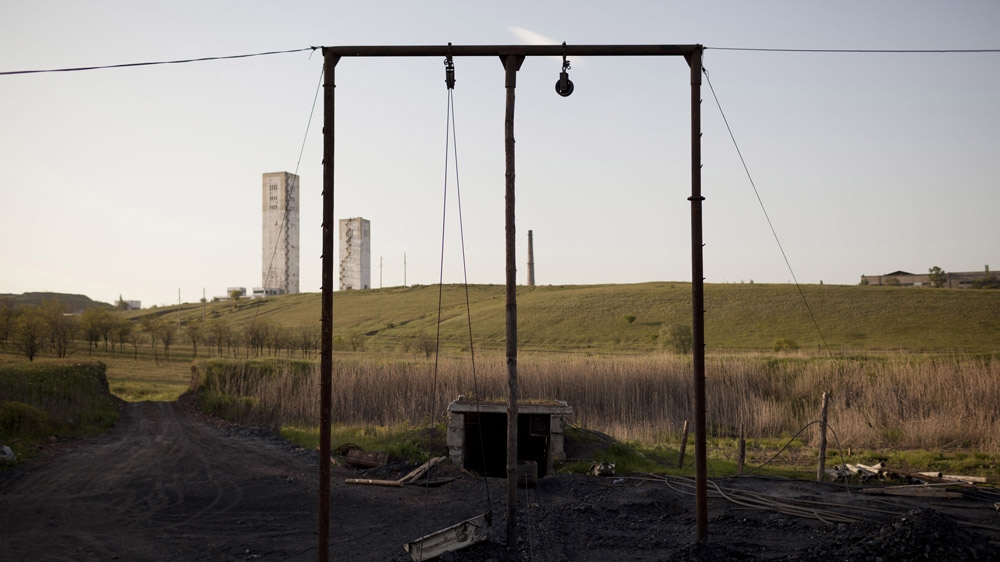 An illegal mine in Davidovka, with the towers of the Glubje mine rising on the horizon. Descending 1,650 metres below the ground, the mine is the deepest in the Donbass. Many miners have died in its tunnels, where temperatures can reach 55 degrees Celsius. [Janos Chiala and Tali Mayer/Al Jazeera] 