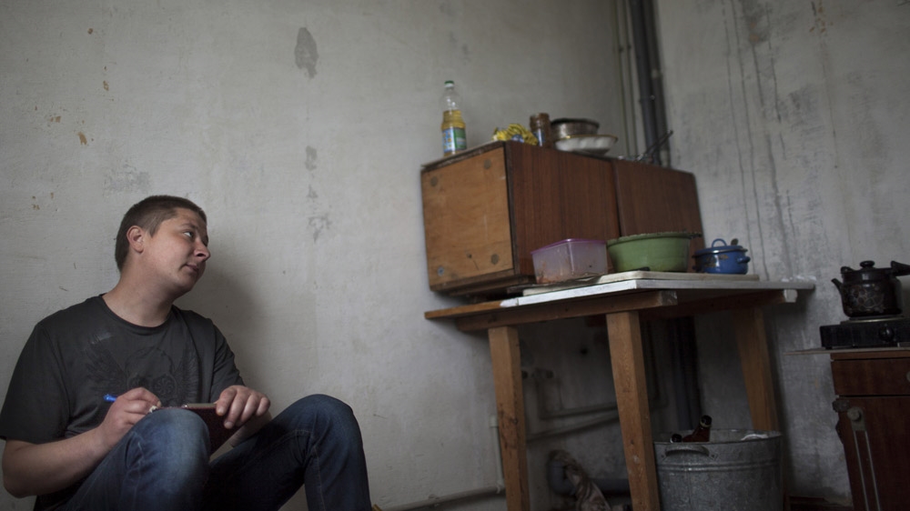 Thirty-year-old Sasha draws in the kitchen of his flat in Shakhtiorsk. He cannot work because of internal injuries he suffered in a mining accident, and therefore has no money. His boss claimed the accident was Sasha's fault and refused to pay him compensation. [Janos Chiala and Tali Mayer/Al Jazeera] 