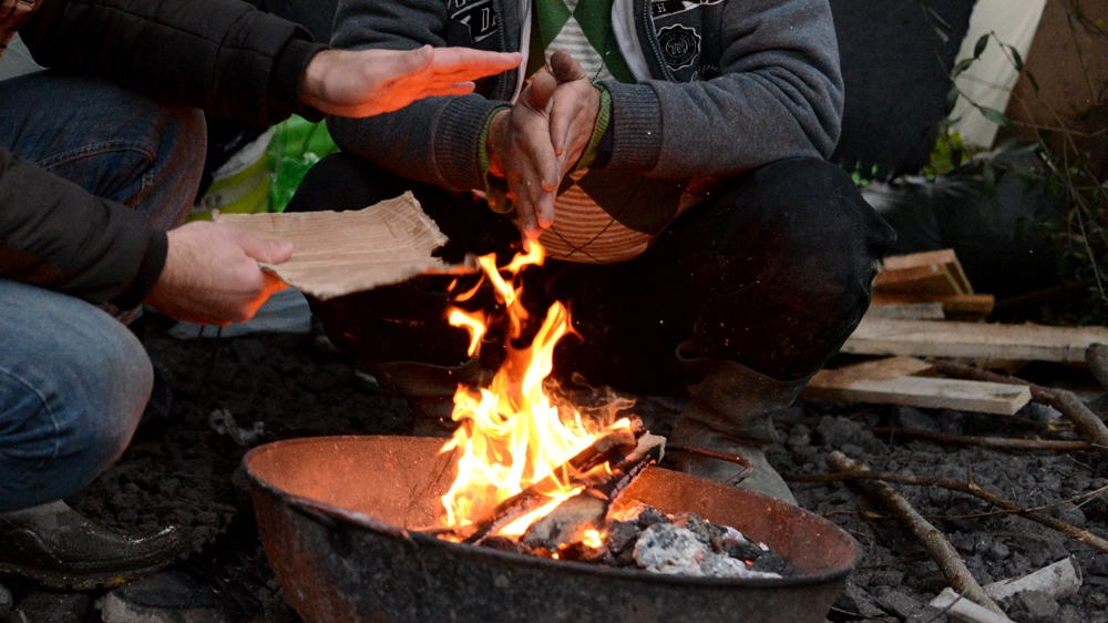 Sarbaz and his brother try to keep warm outside their tent [Lydia Noon/Al Jazeera]