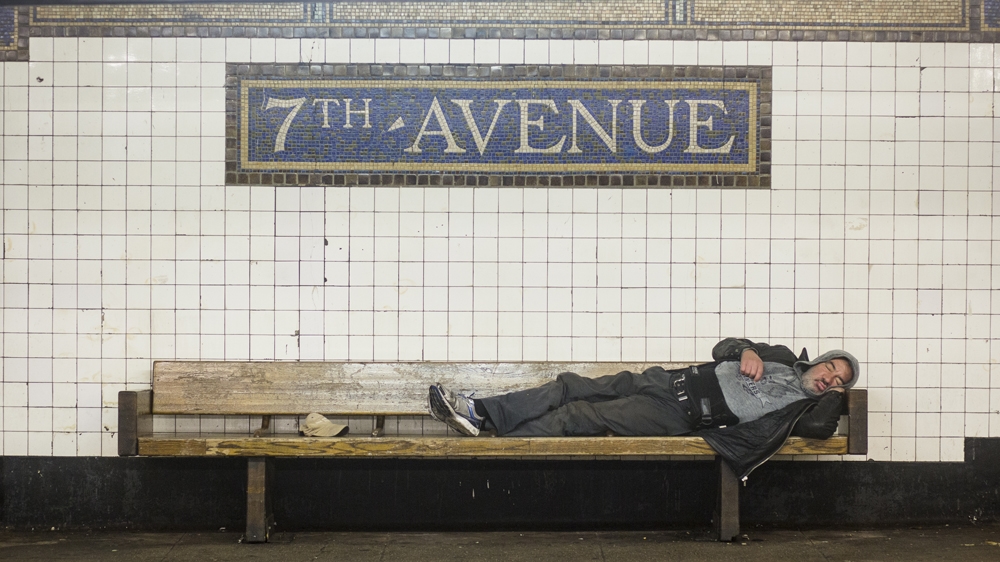 A homeless person sleeps on a subway bench at 7th Avenue station in Brooklyn, New York City [Edu Bayer/Al Jazeera]