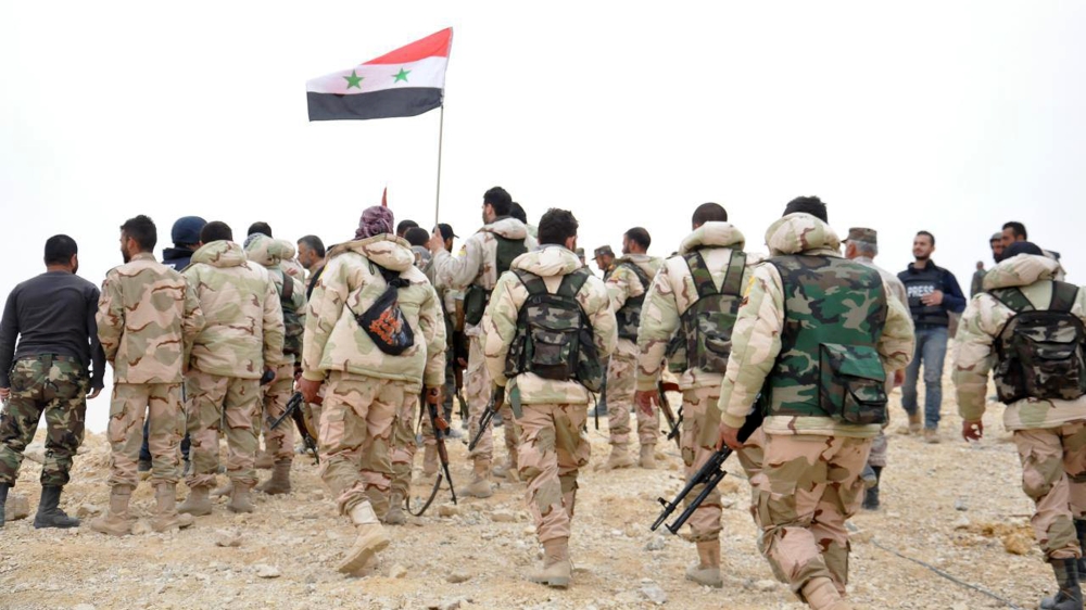 Syrian soldiers gather around a Syrian national flag in Palmyra,