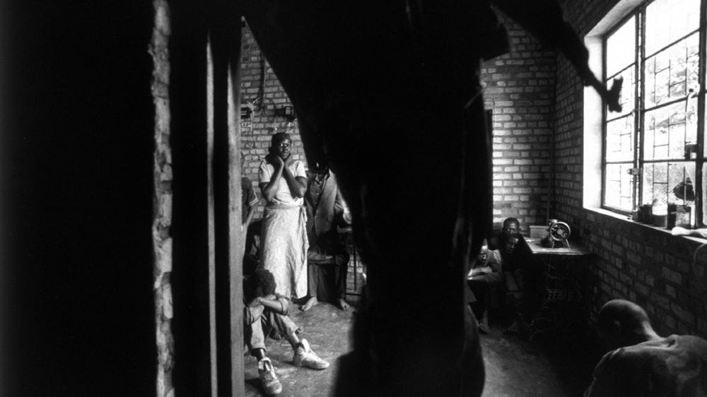 The woman clasping her neck had just confessed to the RPF officer in the doorway to murdering seven Tutsis. She was held with others responsible for mass killings [Jack Picone/Al Jazeera]