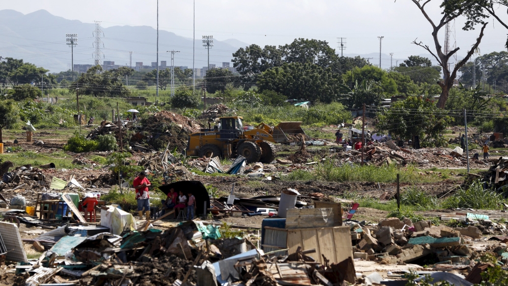 People stand with their belongings next to the ruins of their houses while government officials demolish the remaining houses with a tractor, during a special security operation called "Operation to F