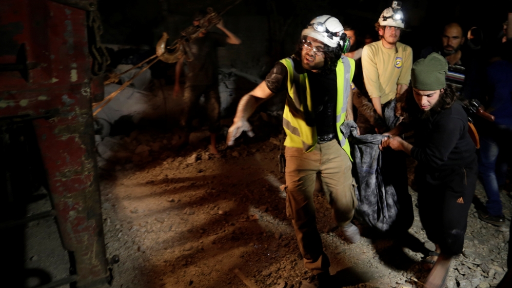 A rebel fighter and civil defence members carry a dead body removed from under debris after Russian air strikes on the Syrian rebel-held city of Idlib