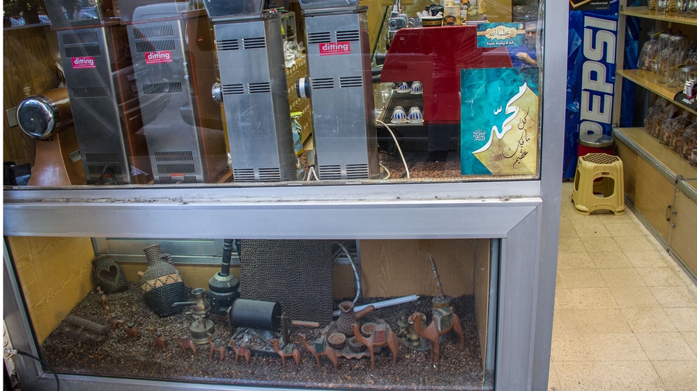 Small wooden camels stand on a desert of brown coffee beans in the showcase in Mohammad Saab's shop [Changiz M Varzi/Al Jazeera]