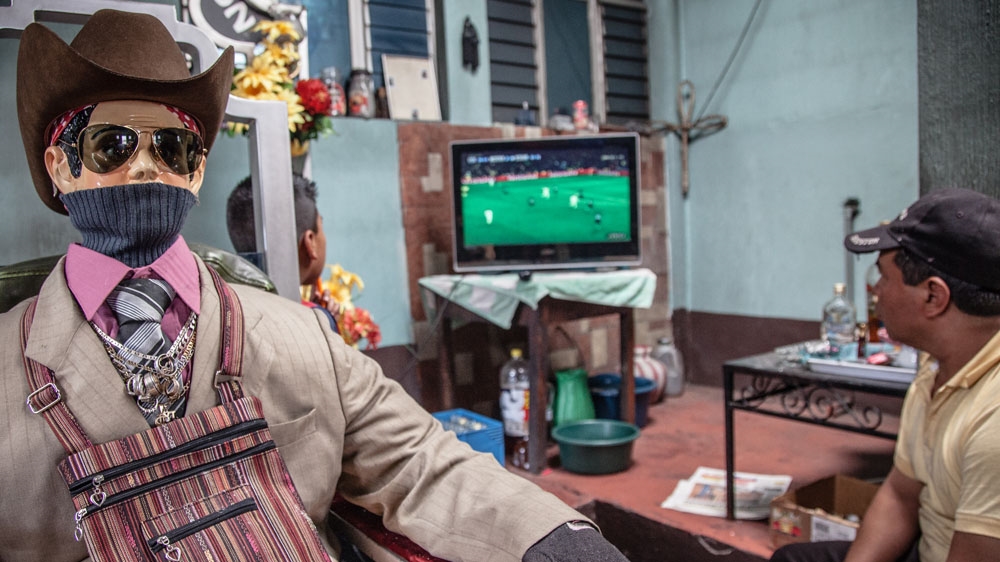 San Simon/Maximon sits behind the shrine along with his attendants. Although there are many variations, he is typically portrayed in a cowboy hat and sunglasses [ Gabriela Campos/Al Jazeera] 