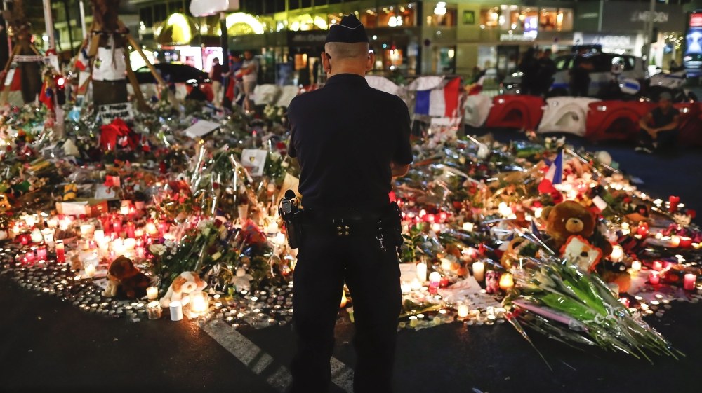 A police officer stands in front of flowers and candles on the Promenade des Anglais where a lorry crashed into the crowd during the Bastille Day celebrations [EPA]