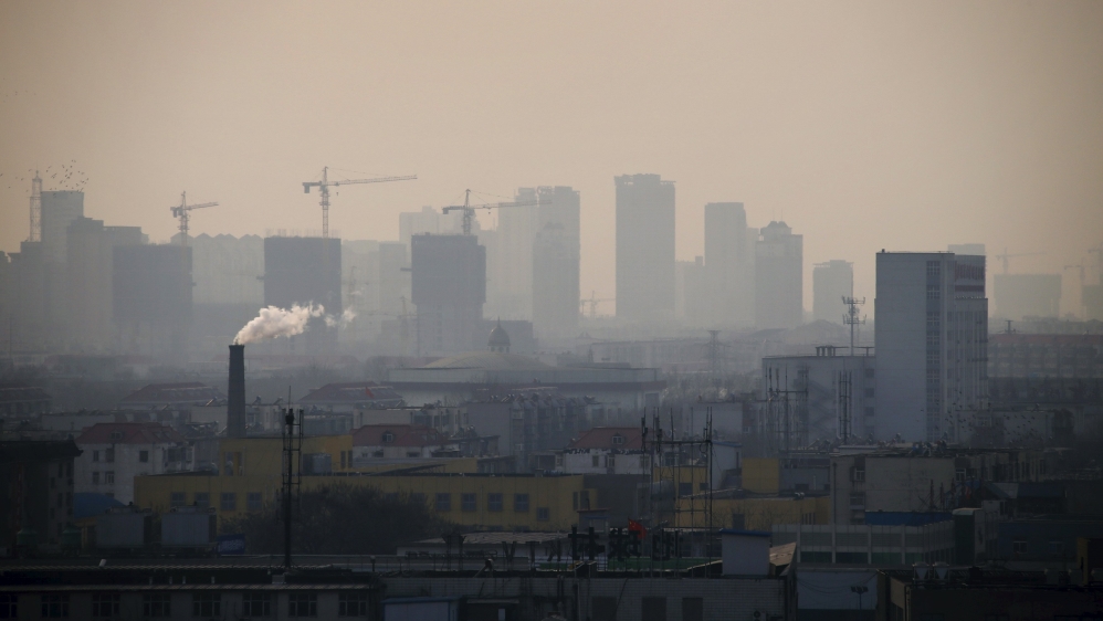 File photo of smoke rising from a chimney among houses as new high-rise residential buildings are seen under construction on a hazy day in the city centre of Tangshan