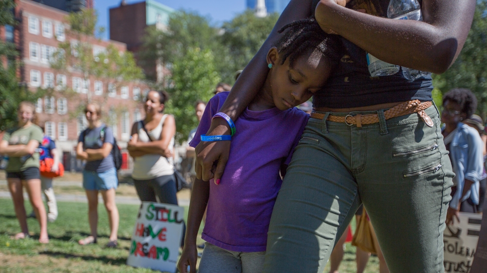 Bria Small, centre, leans against her sister, Naria Sealy, as they listen to Rahsaan Hall speak [Carolyn Bick/Al Jazeera] 