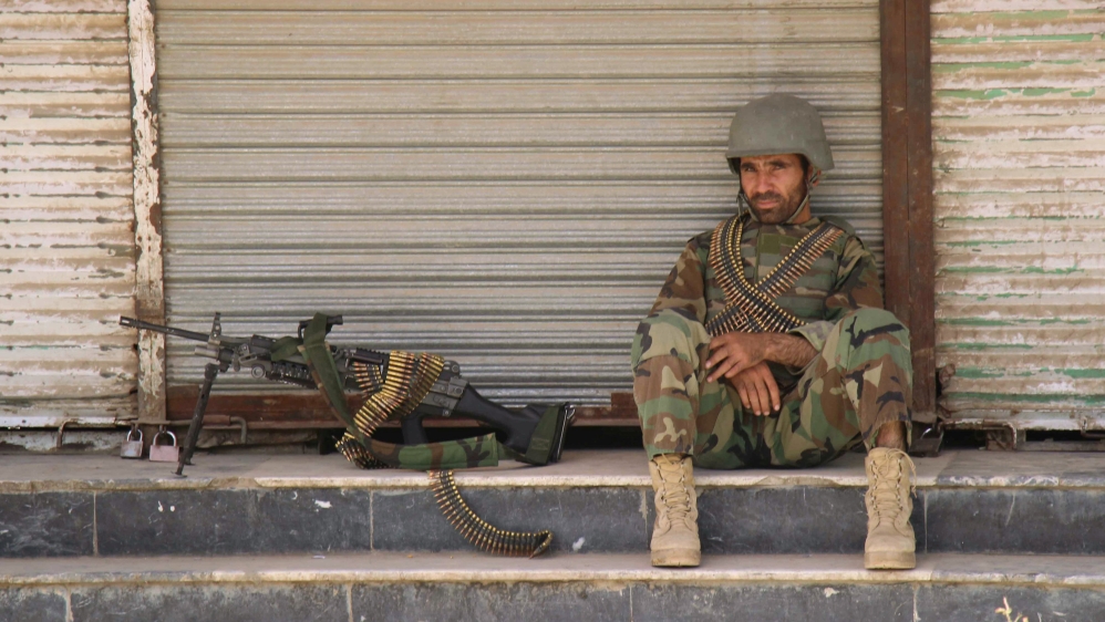 An Afghan National Army soldier sits in front of a closed shop in the downtown of Kunduz city, Afghanistan [REUTERS]