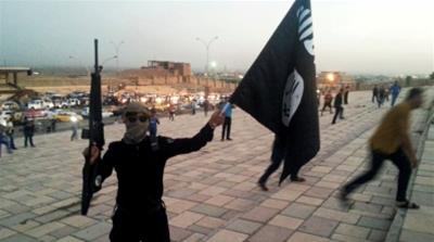 An ISIL fighter holds an ISIL flag and a weapon on a street in the city of Mosul, Iraq [REUTERS] [Reuters]