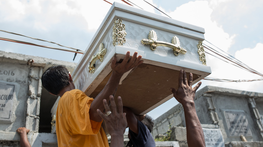 Cemetery workers put the casket of Vicente Batiancila into its temporary burial location. The family received a high interest loan from a loan shark to finance the cost of burial [Paul Ratje/Al Jazeera] 