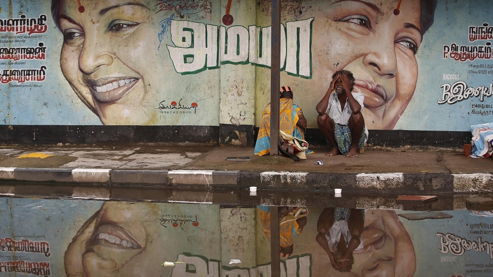 A flood-affected couple sits along a flooded roadside under a picture of Jayalalithaa, CM of Tamil Nadu, in Chennai