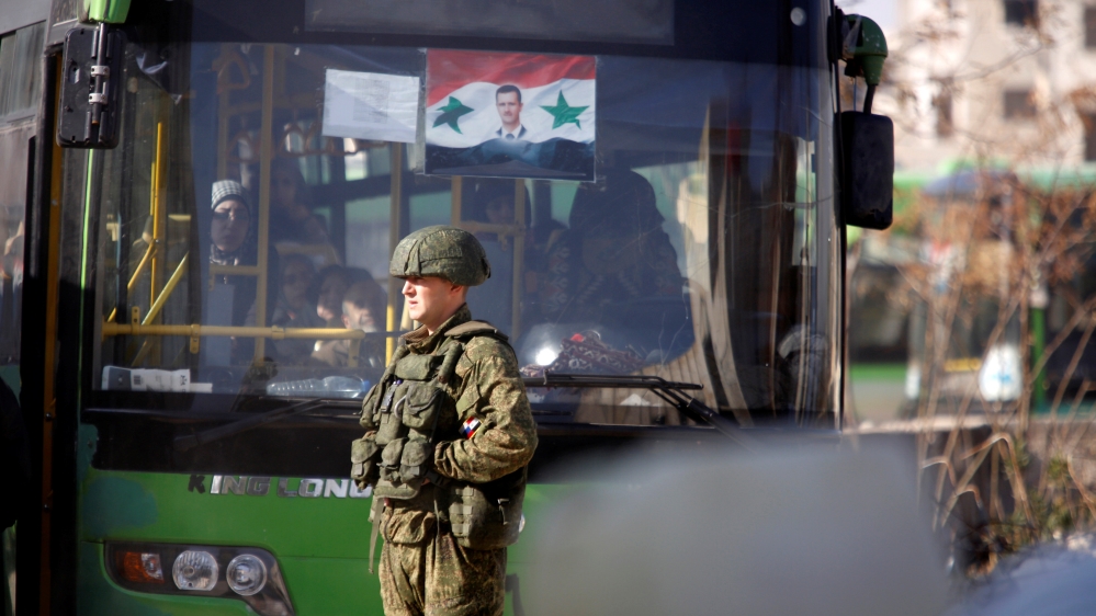 A Russian soldier stands near a bus carrying people who came back to inspect their homes in government controlled Hanono housing district in Aleppo
