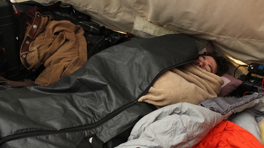 Matthew Snow, a veteran of the war in Afghanistan and a father of young twins, sleeps in a re-purposed body bag [Adam Levinson/Al Jazeera] 