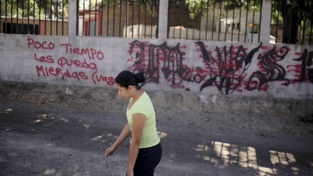 A woman passes by a message threatening gang rivals left on a wall next to MS-13 gang-related graffiti near a crime scene in San Luis Talpa, El Salvador