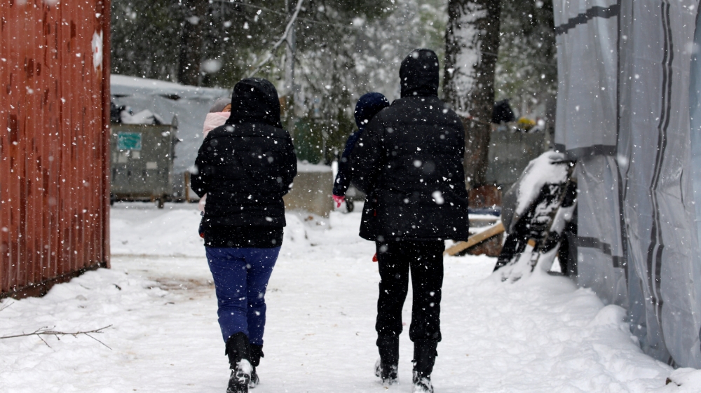 Stranded Syrian refugees carry their children through a snow storm at a refugee camp north of Athens