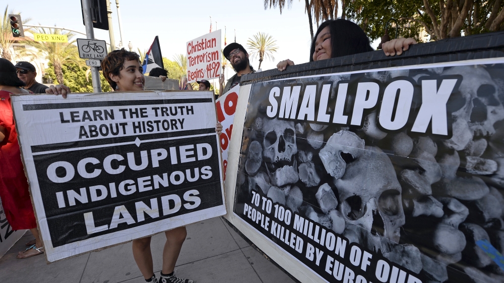 Protesters with signs stand in front of the statue of Spanish missionary Juniper Serra during a protest march by the Mexica Movement organization against Columbus Day in downtown Los Angeles