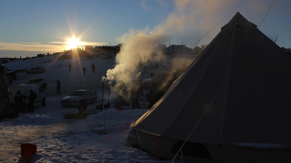 
The sun drops behind Facebook Hill. Wood stoves burn outside, before being moved into teepees and tents to provide heat [Adam Levinson/Al Jazeera] 